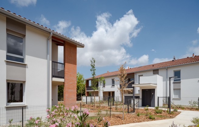 Résidence Le Floréal de logements neufs composée de maisons mitoyennes blanches à toiture en tuiles rouges, avec allées piétonnes, jardins paysagers et ciel bleu partiellement nuageux.