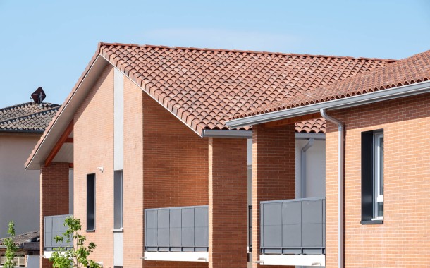 Façades en brique rouge de la résidence Le Floréal contemporain avec balcons aux garde-corps gris et toitures en tuiles sous un ciel bleu clair.